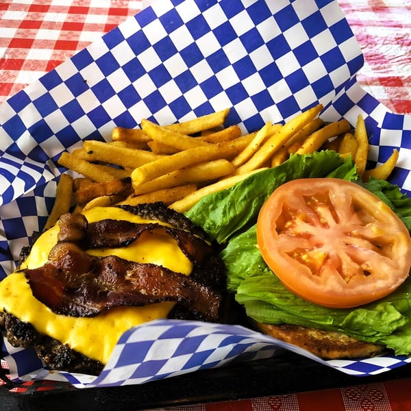 A bacon cheeseburger with fries, lettuce, and tomato in a blue and white checkered basket.