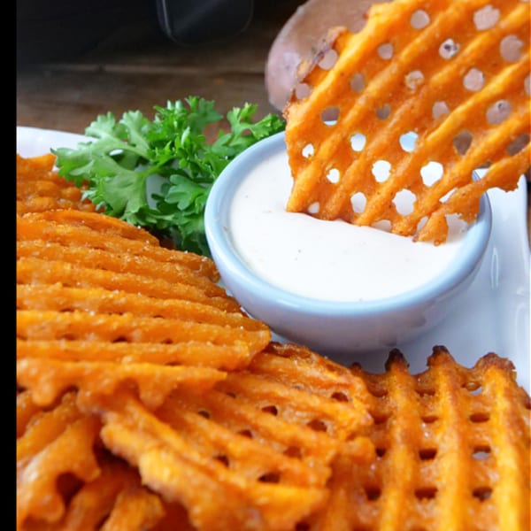 Crispy sweet potato waffle fries with a side of creamy white dipping sauce and fresh parsley.