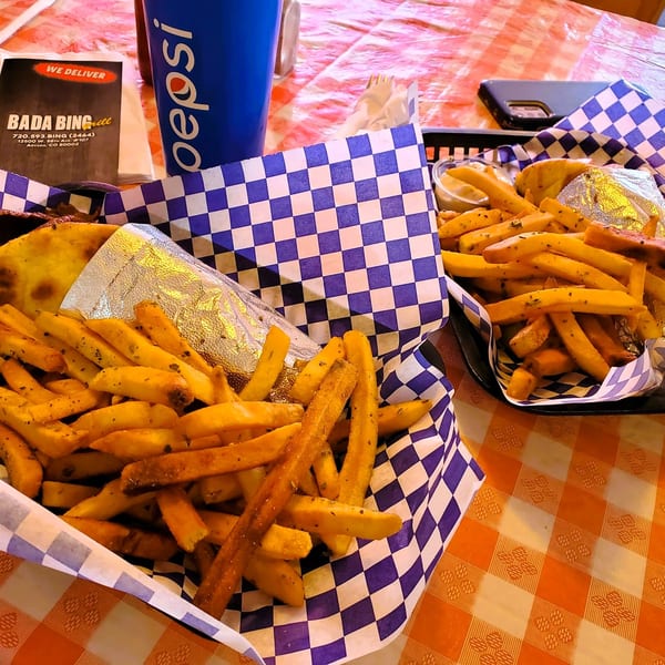 Two baskets of seasoned fries and a wrapped gyro on a checkered table with a Pepsi cup.
