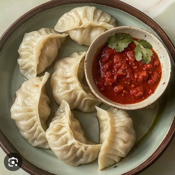 A plate of steamed dumplings with a side of red chili sauce, garnished with cilantro.