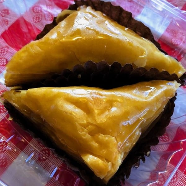Two pieces of baklava, glistening with honey, in brown paper liners on a red and white checkered surface.